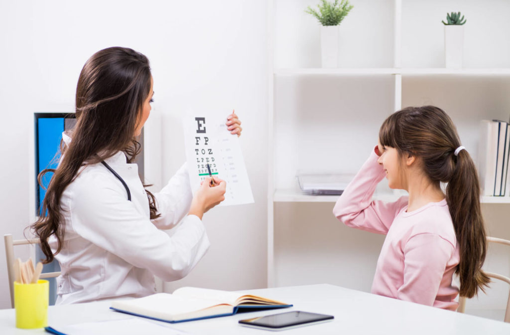 An optometrist holding an A4 size Snellen chart during a girl's eye exam in the clinic.