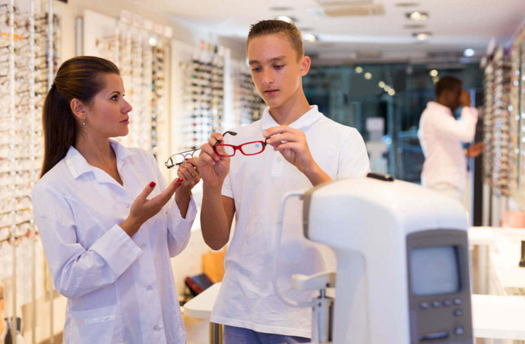 A female optician is helping a teenage boy choose the eyeglasses he fits well.
