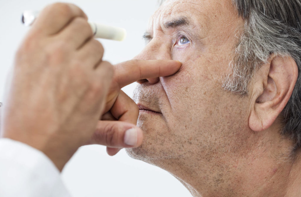 An eye doctor is examining the eye of an elderly patient with the use of a pen light.