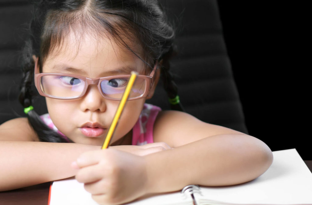 A young girl with strabismus is doing her homework.