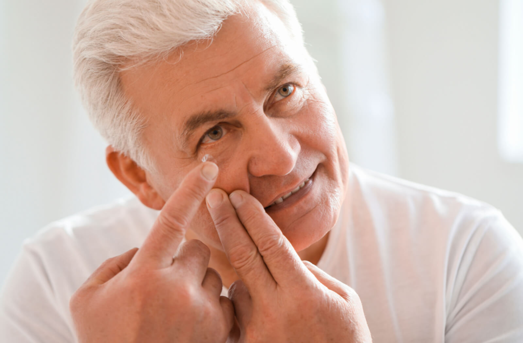A senior man putting on a single toric contact lens on his right eye to correct his astigmatism.