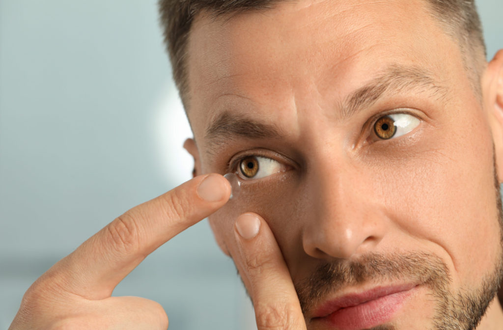 A close-up of a man putting a contact lens on his right eye.