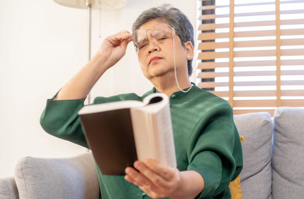 A woman adjusting her glasses and holding her book further from her to read better.