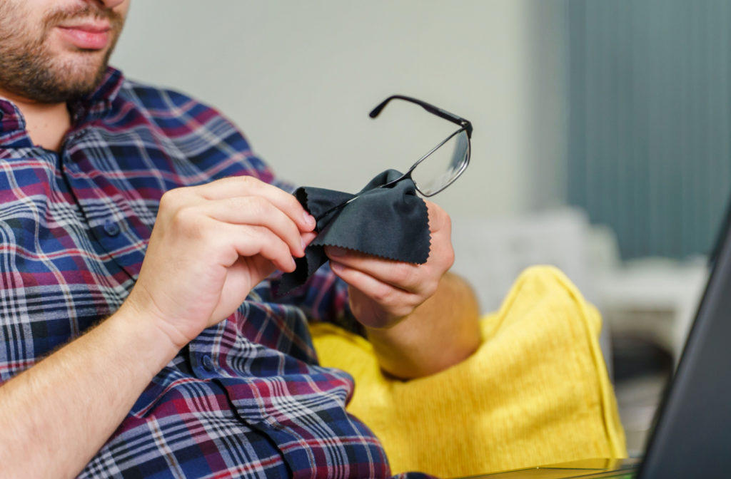 A man in a checkered shirt cleaning his bifocal glasses with a black microfiber cloth.