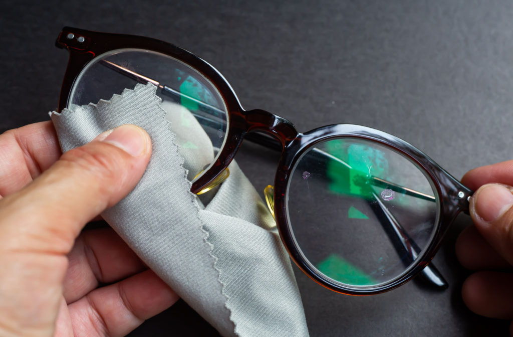 A close-up of a pair of reading glasses being cleaned using a microfibre cloth.