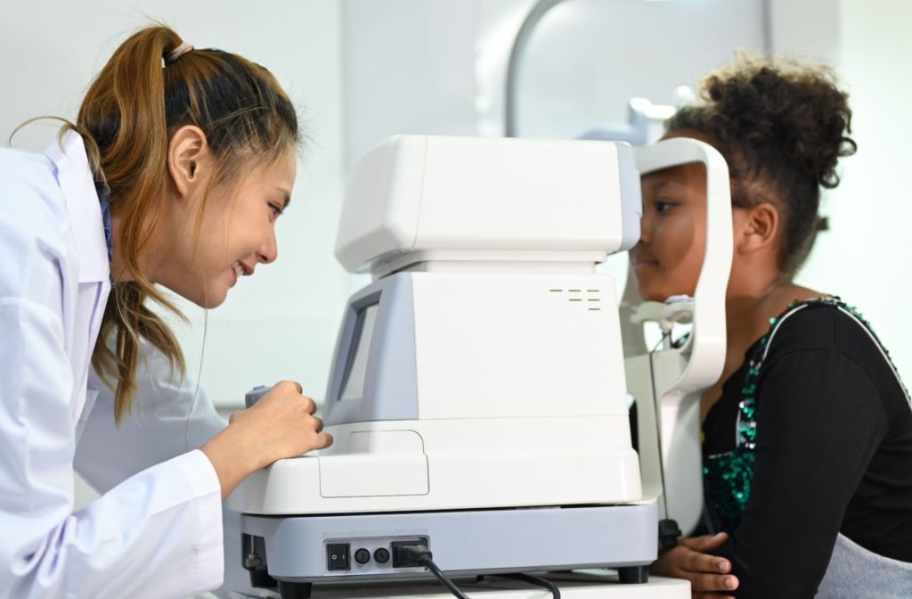 A child sits in front of an auto refractor machine while their optometrist examines their eyes for astigmatism.