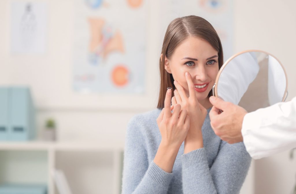 An optometrist holds up a mirror for their patient to practice putting on their contacts.