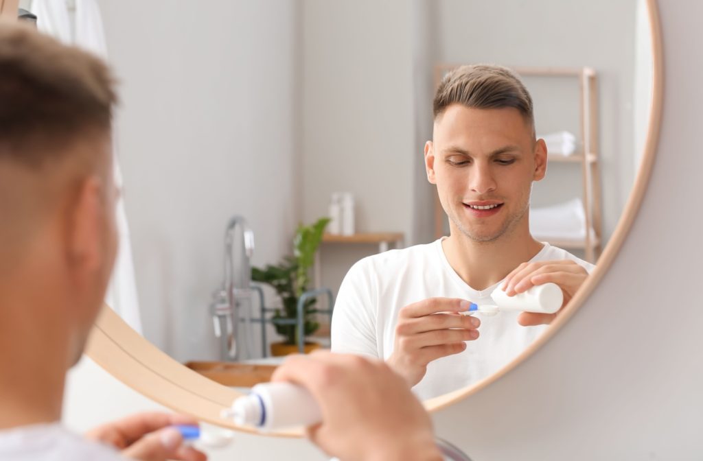 A person standing in front of a mirror in a brightly lit room holding a contact lens case and applying solution to their contact lenses for proper storage.