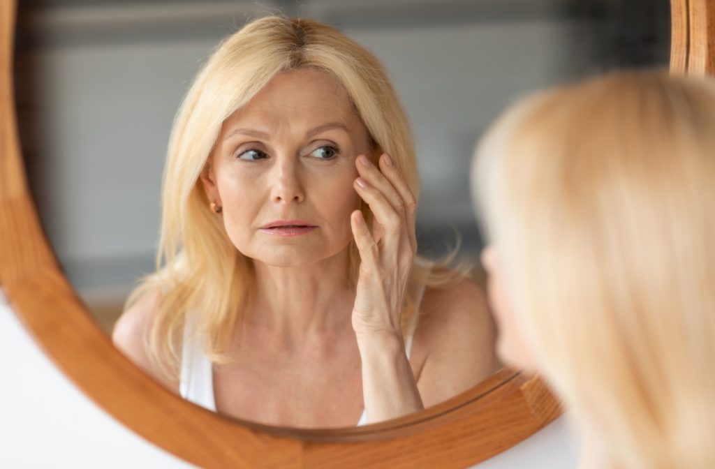 An older woman closely examining her eyes in the mirror, observing them with care and attention.