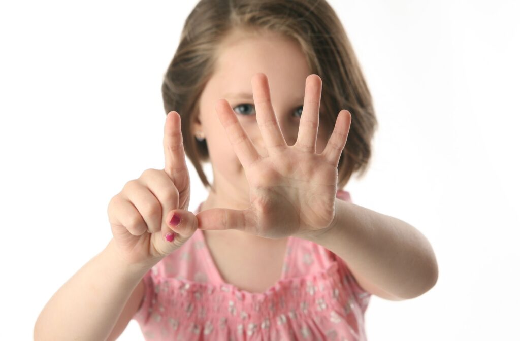 A young child holding up 6 fingers in front of their face.