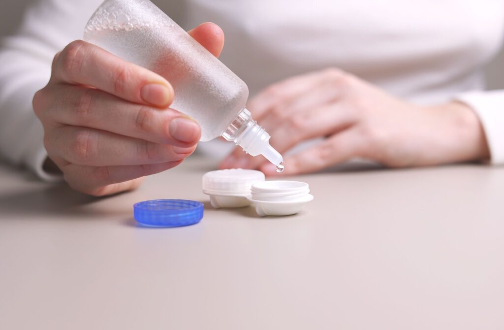 A hand dropping contact lens solution into a contact lens case.