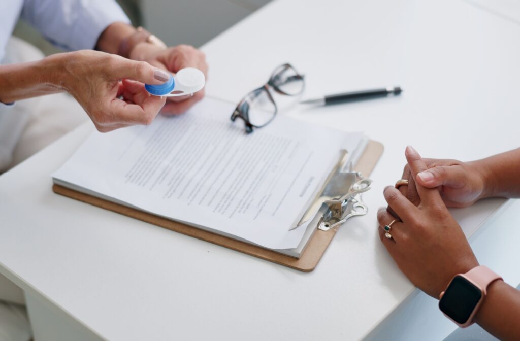 A desk with glasses, a contact lens case, and notepad with a contact lens prescription at an optometry office.