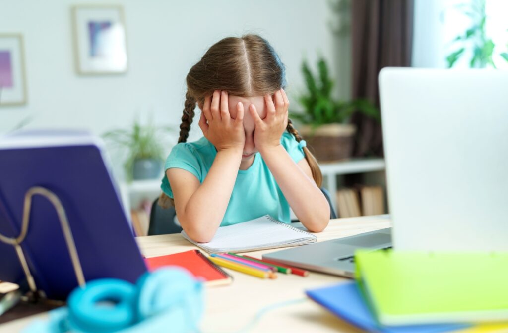A child rubbing their eyes due to vision problems while doing school work at a desk.