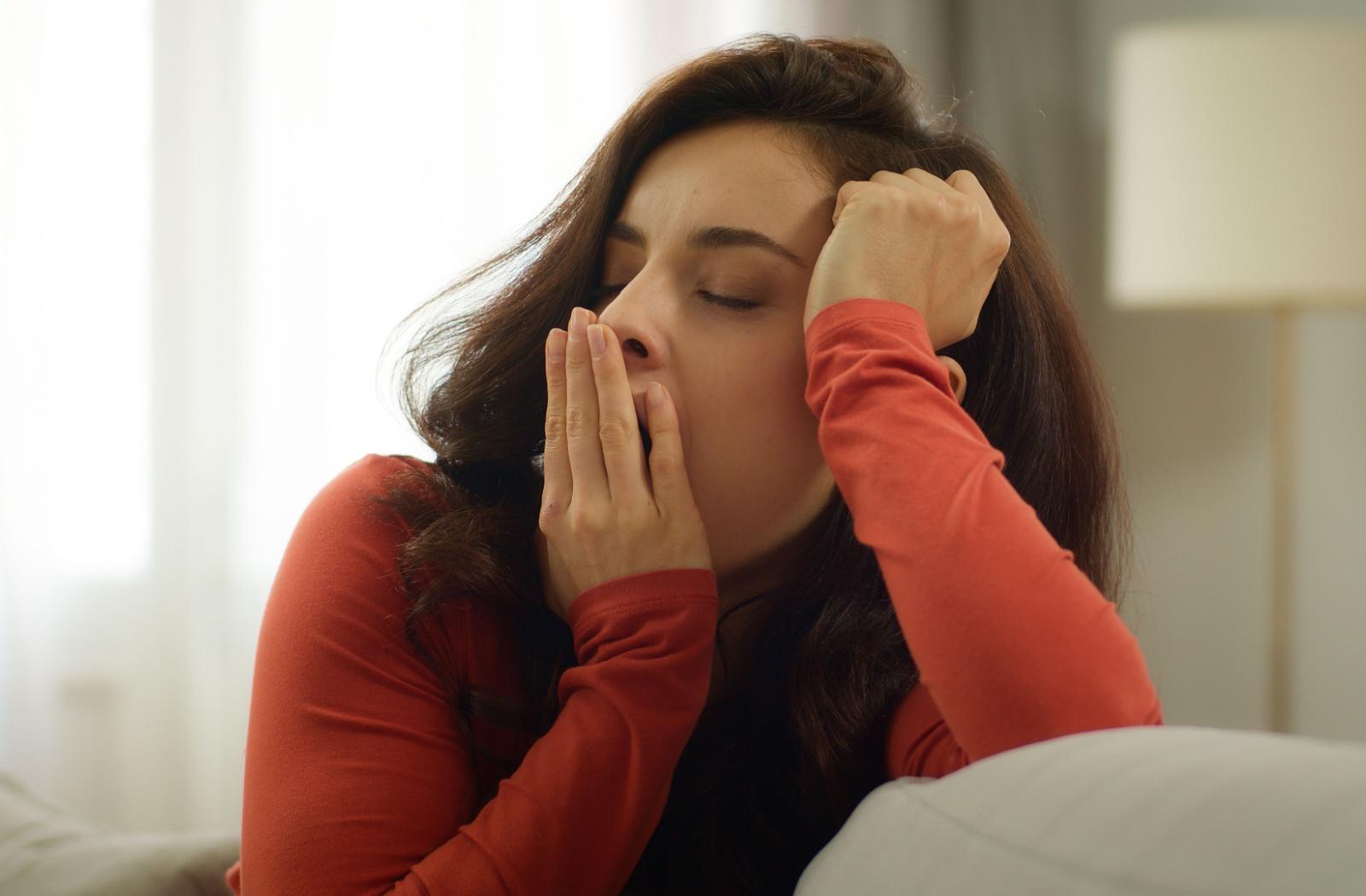 A tired person yawning while sitting on a couch.